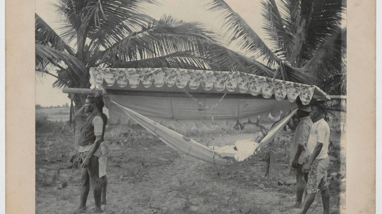 Unbekannter Fotograf; Vier afrikanische Männer, eine Europäerin in einer Hängematte mit Baldachin tragend, Togo, 1890–1920